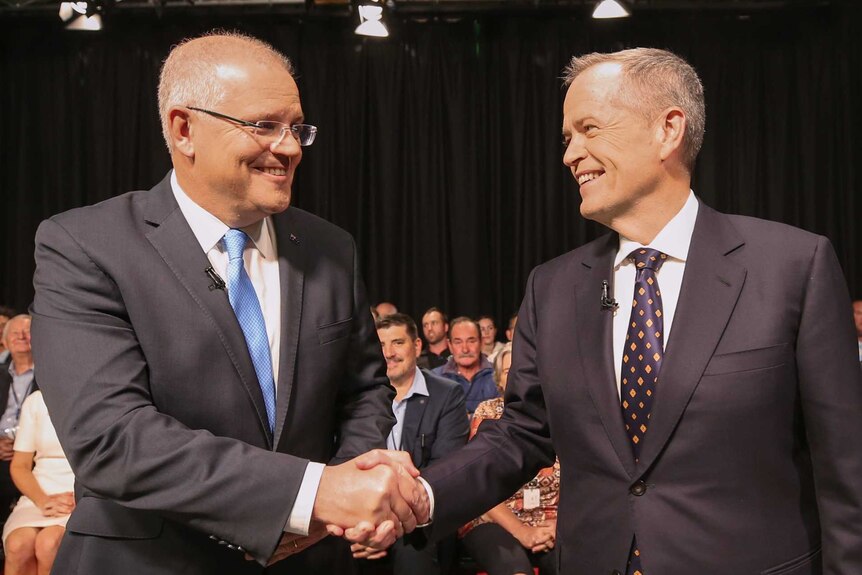 Scott Morrison, left, shakes hands with Bill Shorten, right, as they look into each other's eyes. A crowd is seated behind them.