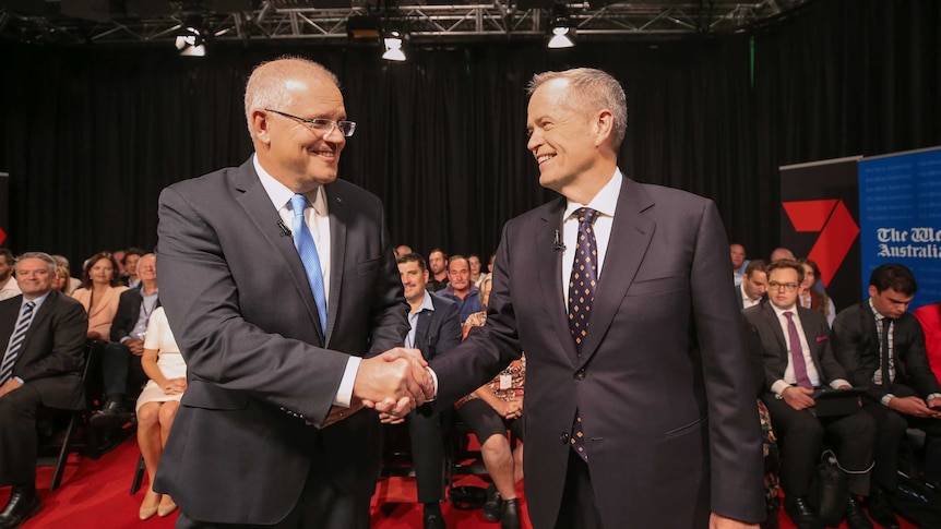 Scott Morrison, left, shakes hands with Bill Shorten, right, as they look into each other's eyes. A crowd is seated behind them.