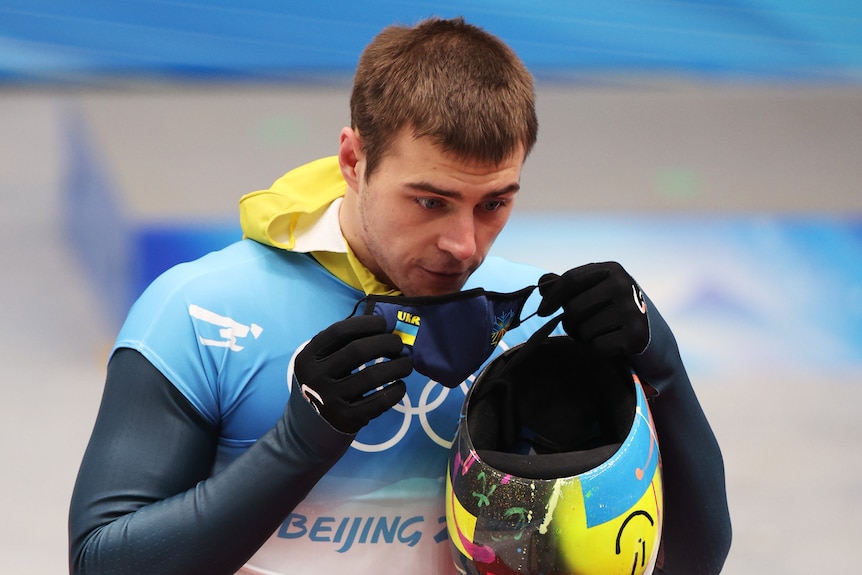 Ukrainian skeleton racer Vladyslav Heraskevych puts on a facemask at the Beijing Winter Olympics.