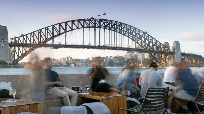 People sit at a bar overlooking the Sydney Harbour Bridge.