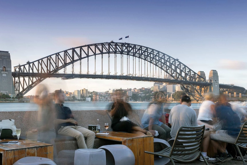 People sit at a bar overlooking the Sydney Harbour Bridge.