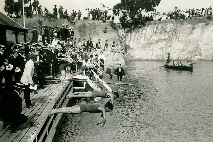 A black and white photo of swimmers diving into the water at Surrey Dive in the 1900s.