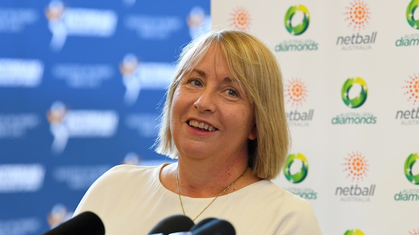 Lisa Alexander smiles sitting at a desk with a microphone in front of her