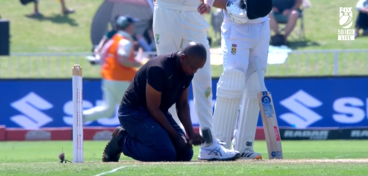 A man in dark clothing hammers down a cricket pitch with a mallet
