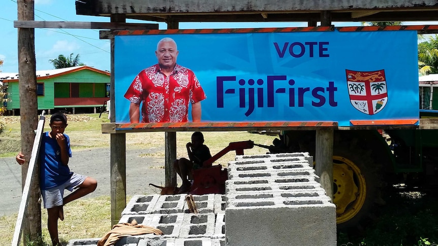 A young boy stands beside a colourful poster promoting current Fiji PM Frank Bainimarama