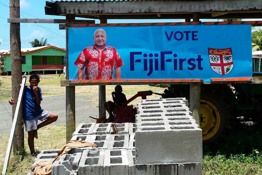 A young boy stands beside a colourful poster promoting current Fiji PM Frank Bainimarama