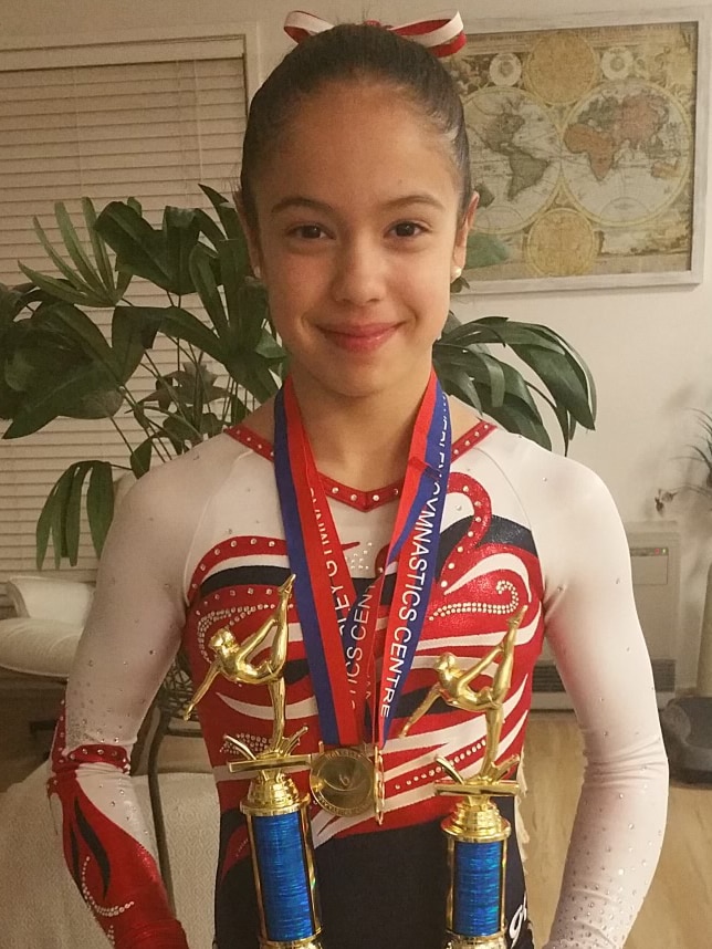 Scarlett Magnanini holds two large trophies and smiles for the camera.