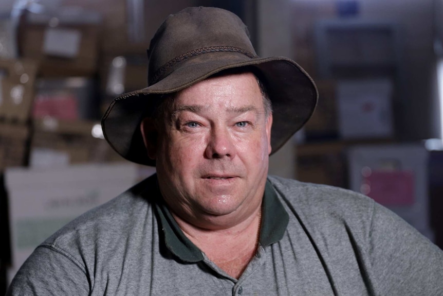 MCU of builder, Rod Grieve, wearing battered sun hat and green collared polo shirt.