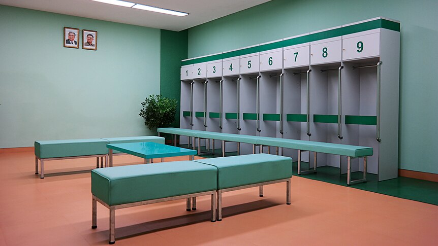 A flurorsecent light lit locker room with mint green coloured walls and peach coloured floors.