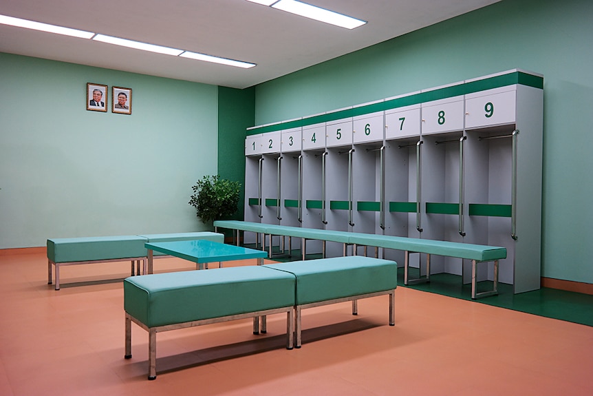 A flurorsecent light lit locker room with mint green coloured walls and peach coloured floors.