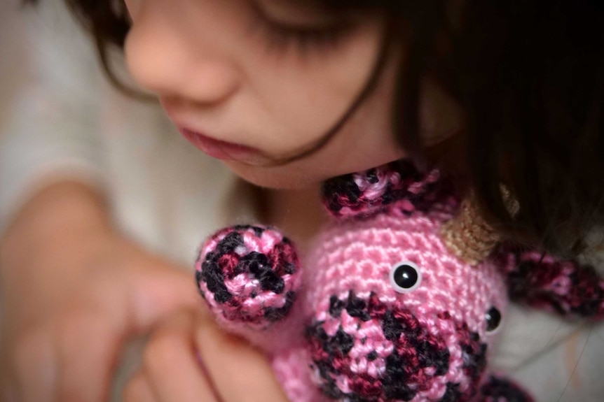 A child hugs a crocheted unicorn soft toy
