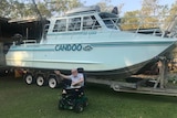 Paralysed man in wheelchair in front of modified fishing boat.