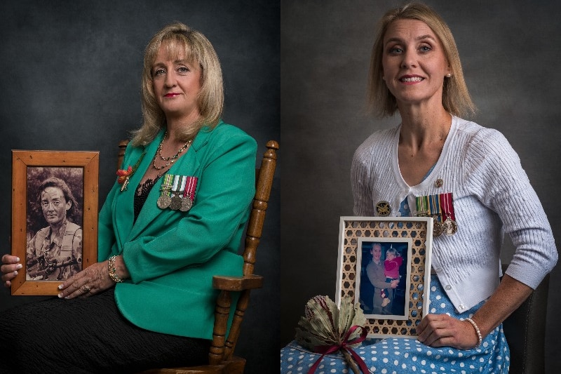 Two women wearing service medals sit in chairs while holding framed photographs