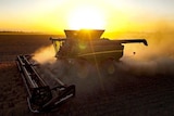 A harvester is silhouetted against the setting sun.