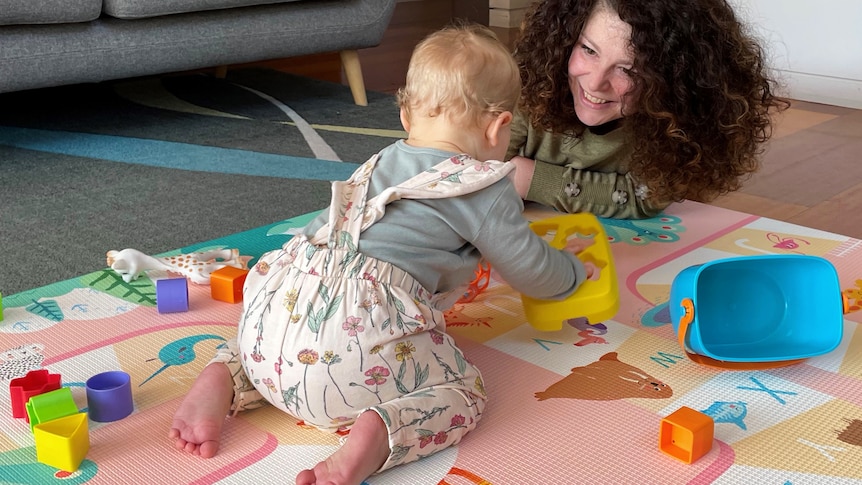 A young girl plays with colorful plastic toys on a rug with her mum.