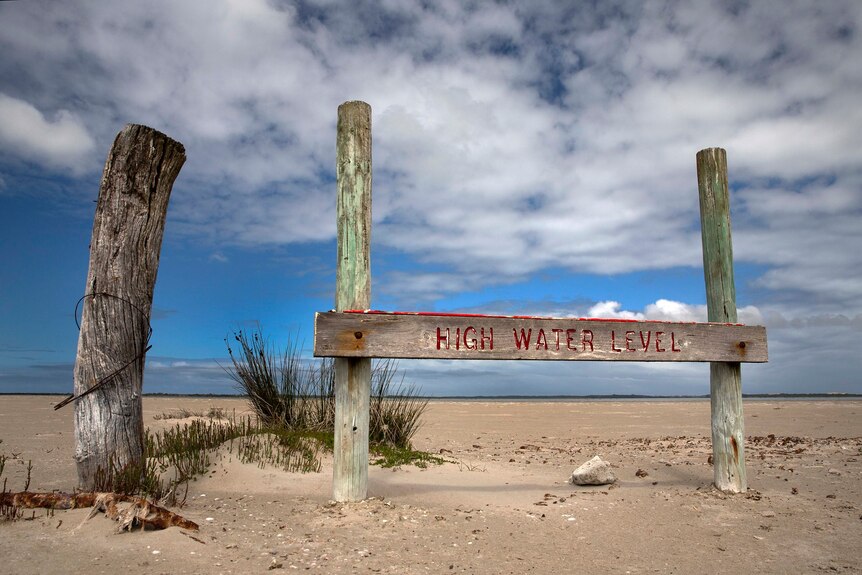 A sign reading 'high water level' in the sand, at the bottom of an empty lake