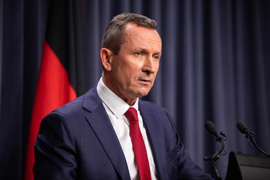 A man in a blue suit and red tie stands at a podium