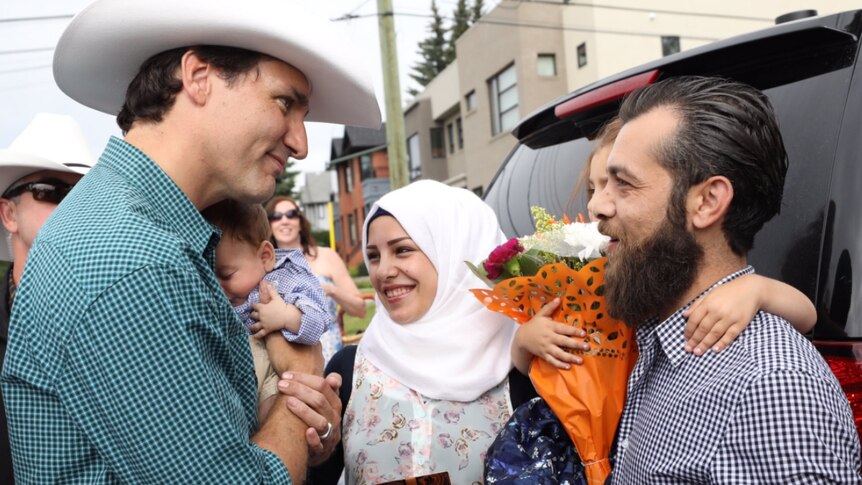 Justin Trudeau holds baby while talking to a family from Syria.