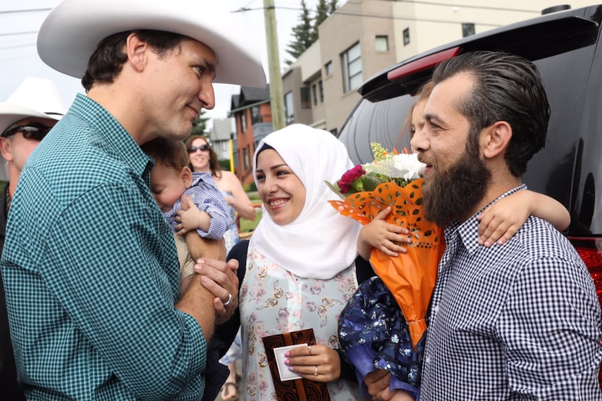 Justin Trudeau holds baby while talking to a family from Syria.