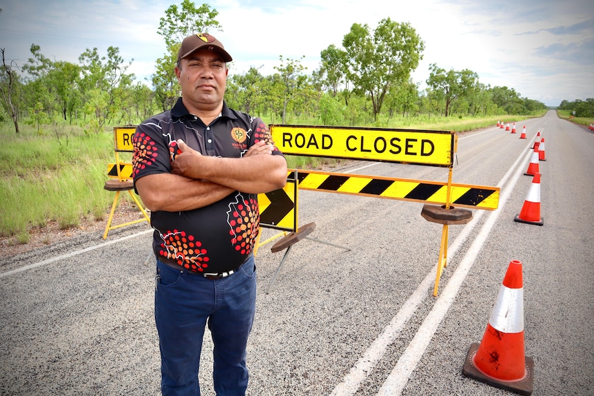 a man wearing a collared shirt with indigenous prints standing on a road with orange cones around him