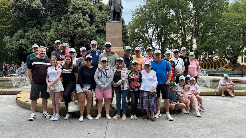 A large family group stands in a town square in front of fountain.