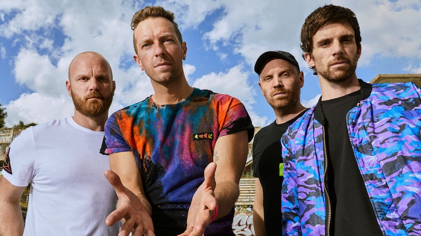 four men in t-shirts, with a blue sky and clouds above them.