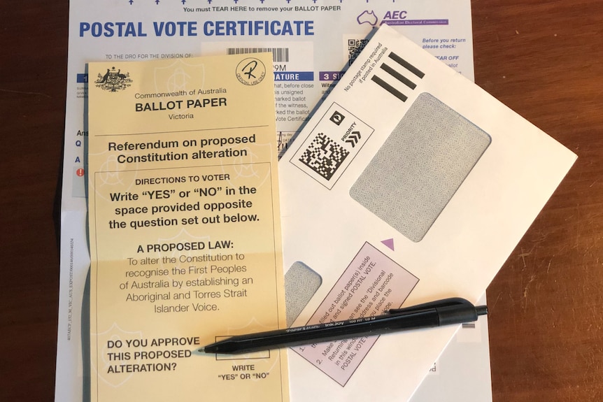 A ballot paper for the Voice to Parliament sitting on top of a postal vote certificate and envelop with a pen.