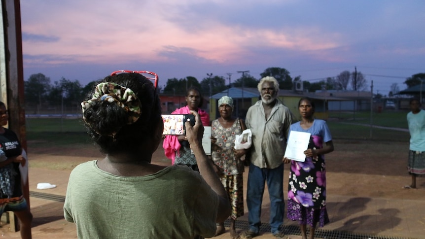 A woman takes a photo of four graduates