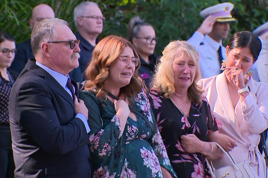 A group of four people standing in front of saluting paramedics, clearly overwhelmed with emotion.