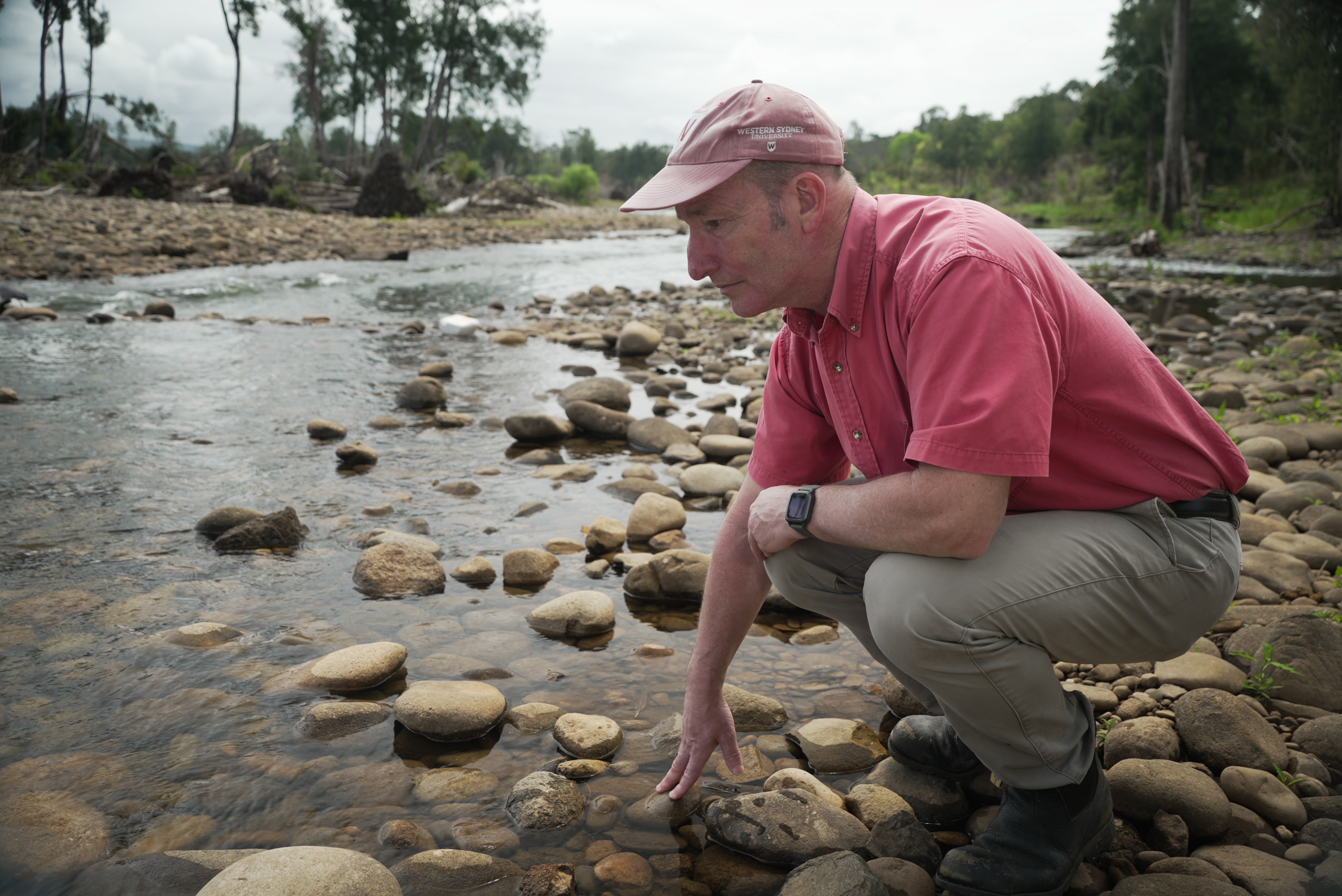 A man kneels in a creek looking down