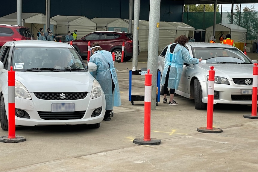 Cars line between orange traffic poles as vaccination workers in full PPE deliver vaccines.