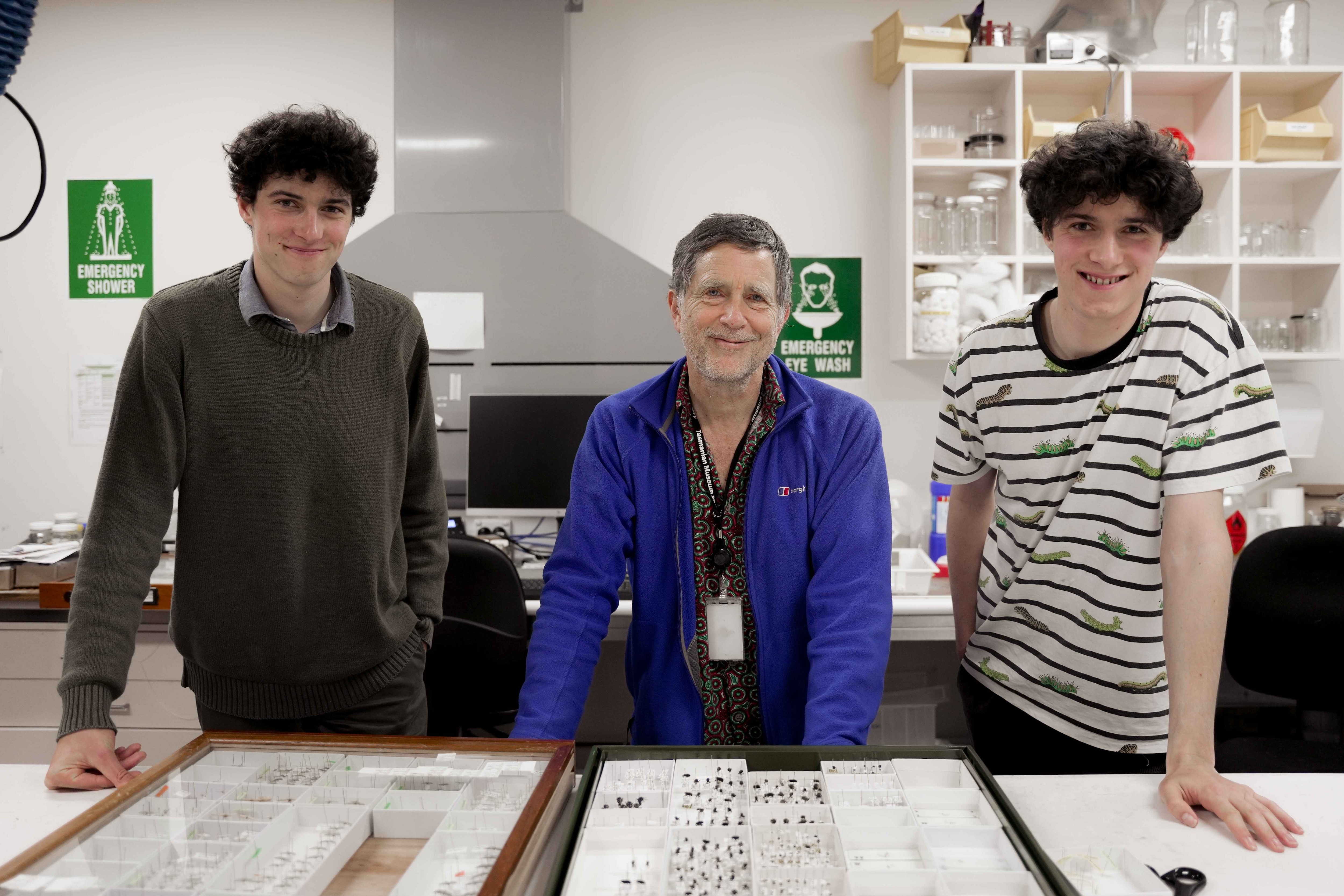 Three men smile for a photo in a science lab.