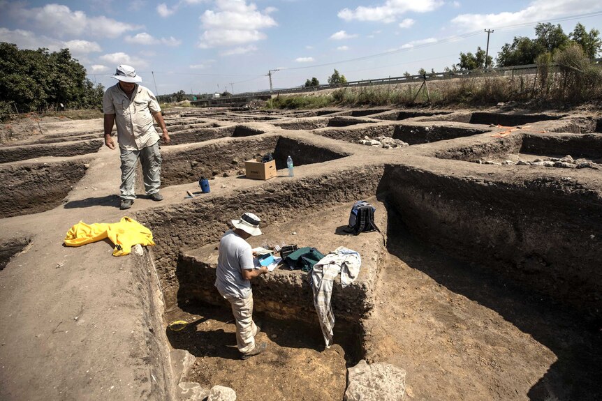 Archaeologists stand on and work in an excavated site.