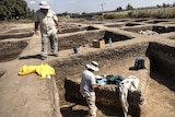Archaeologists stand on and work in an excavated site.