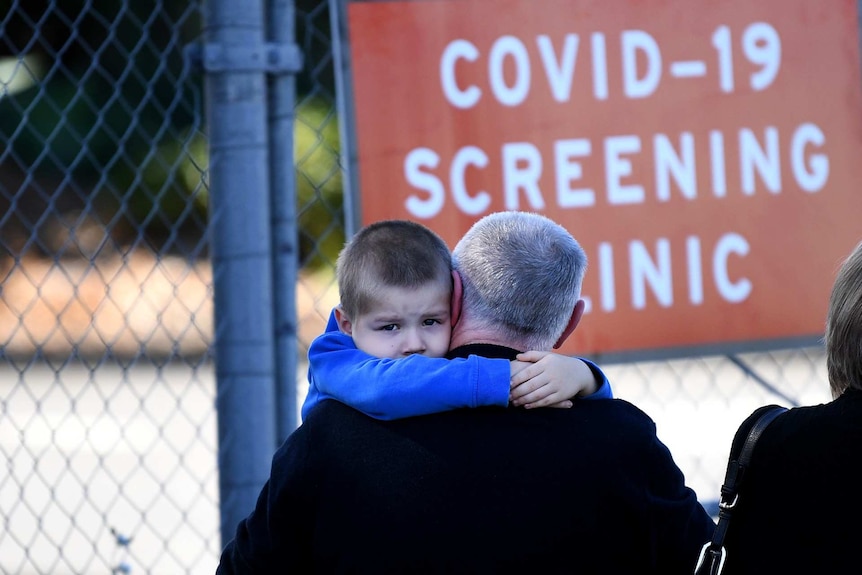 A boy looks worried as he waits to be tested for coronavirus in front of a sign that reads "COVID-19 screening clinic".