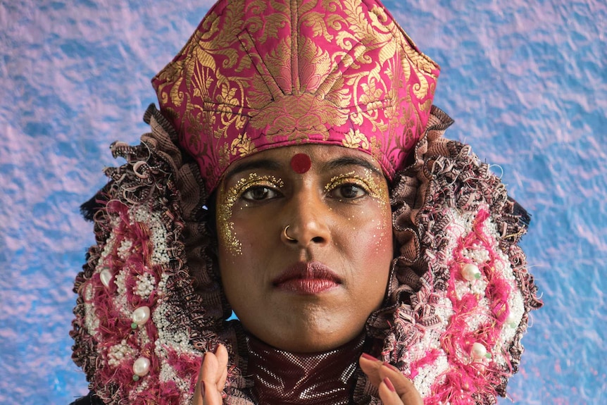 Hindu model wearing pink and purple headdress and shiny clothing.