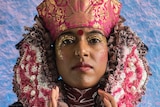Hindu model wearing pink and purple headdress and shiny clothing.