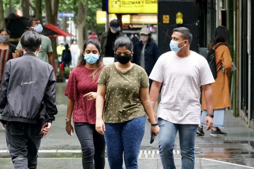 About a dozen people, all wearing masks, crossing a busy intersection.