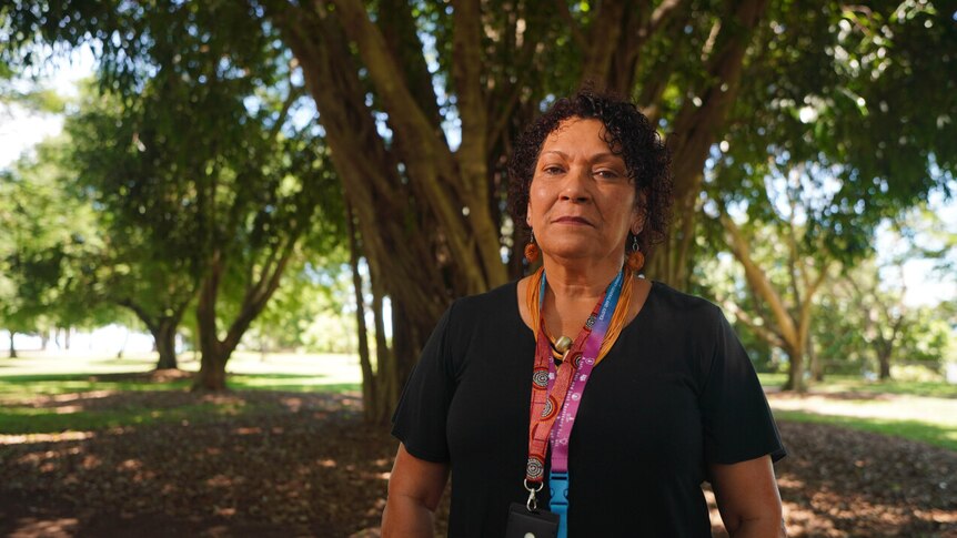 Woman stands in front of tree with lanyard around neck 