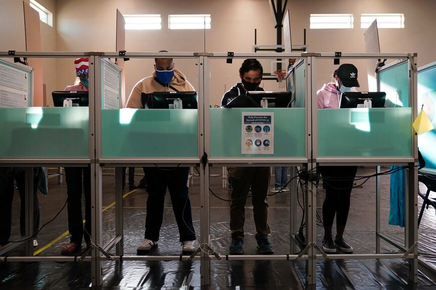 Four voters wearing face masks vote in private booths.