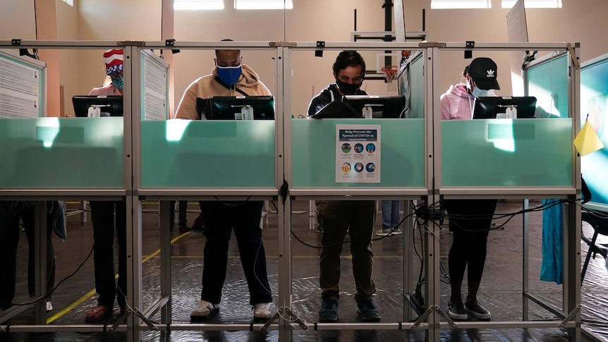 Four voters wearing face masks vote in private booths.