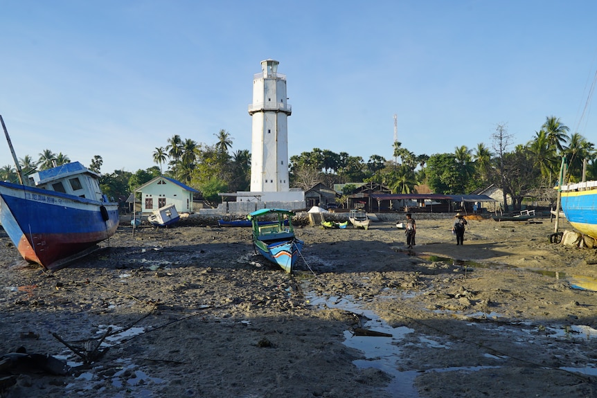 A boat on the brown sandy shore in West Timor's island of rote where a white lighthouse stands tall in the background. 