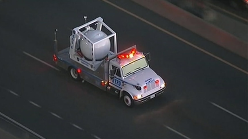 A truck carrying a large metal container drives on a highway.