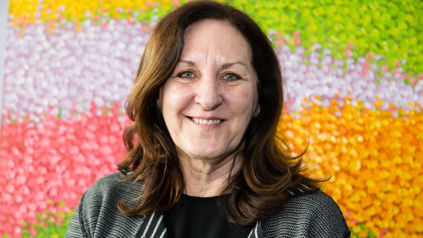 A woman poses in front of a colourful artwork.