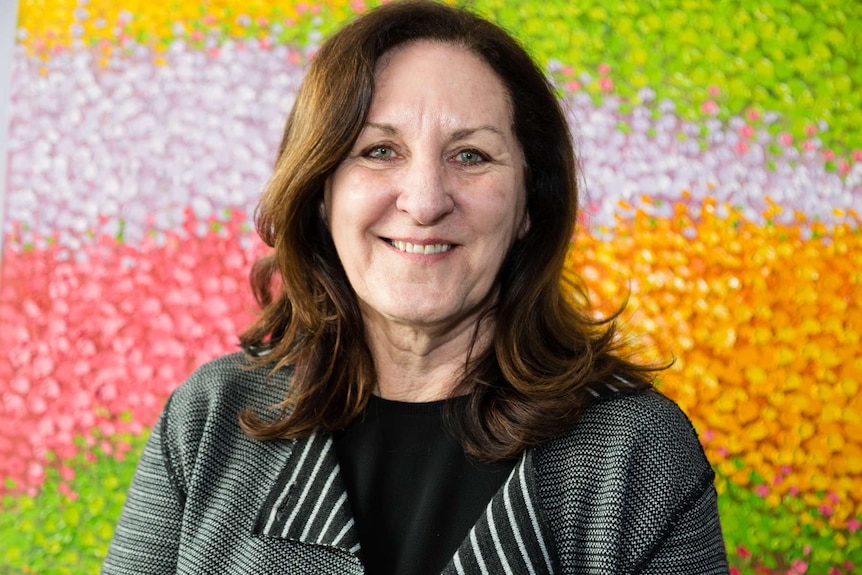 A woman poses in front of a colourful artwork.