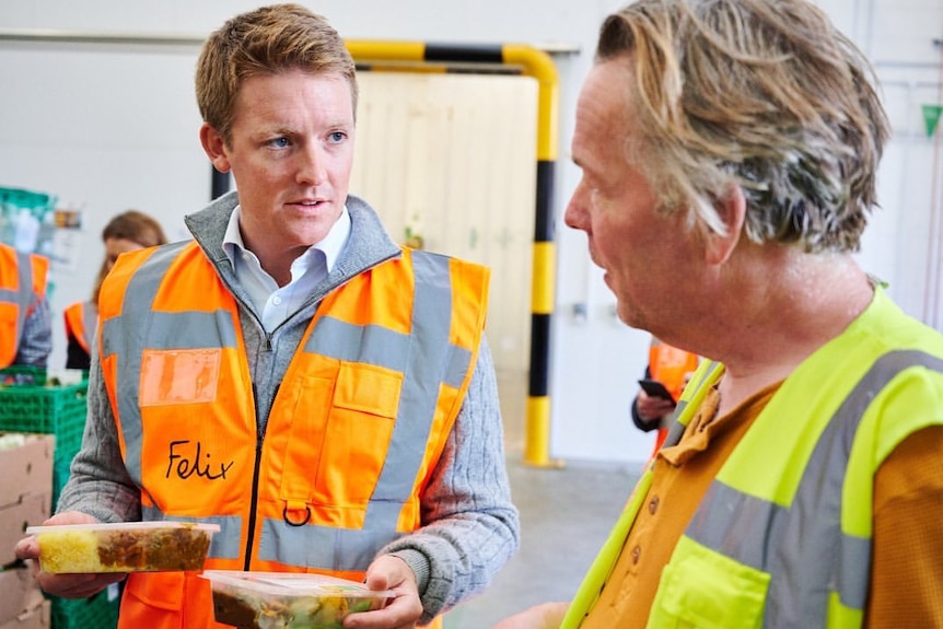 A close up of a man wearing a high vis orange shirt talking to a man in a yellow vest.