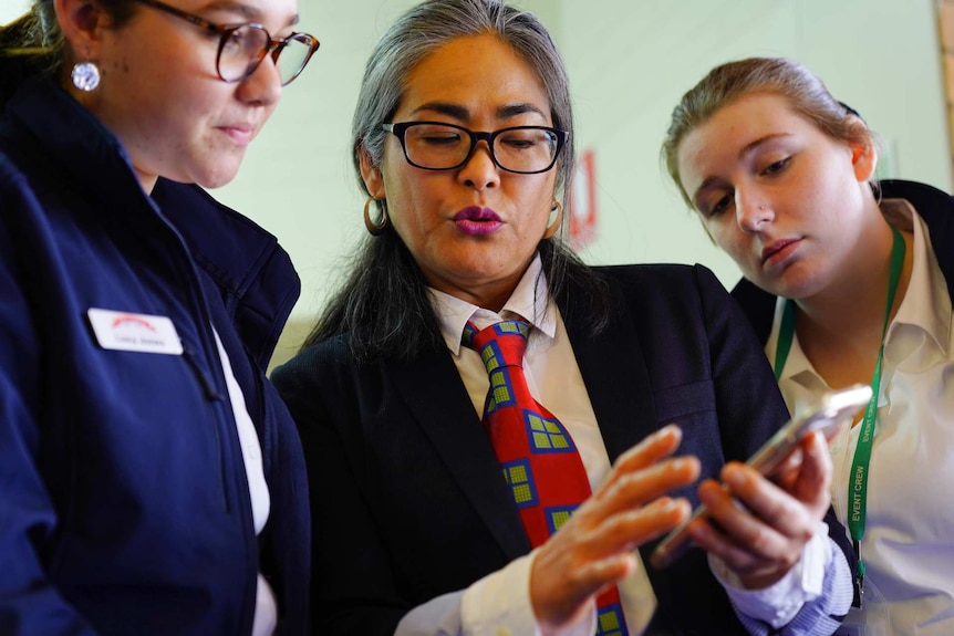 A woman looks at a mobile phone with two younger women.