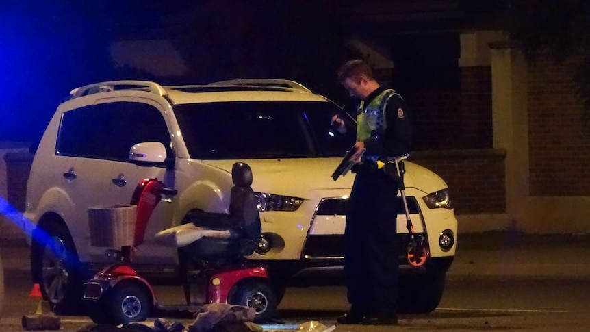A police officer stands in front of a damaged car and mobility scooter