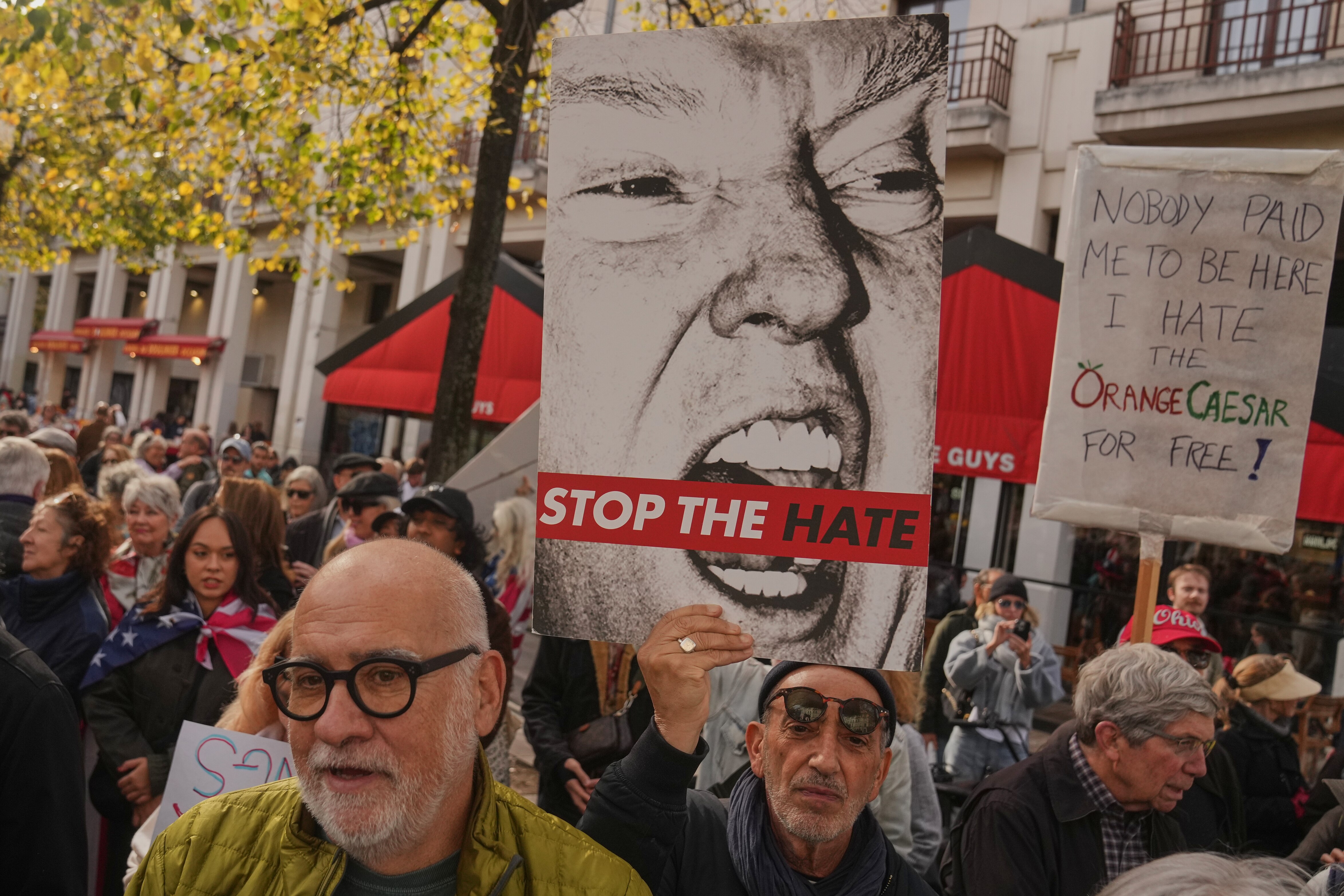 A man holding up a grey image of Donald Trump's face with 'Stop The Hate' across it in red, during a protest