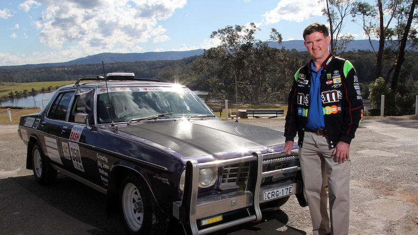 Brian Muller stands in front of his Variety Bash car with Shoalhaven River in the background.